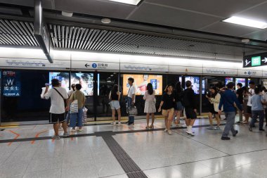Deniz Kuvvetleri, Hong Kong - 28 Ağustos 2024: Mtr tren istasyonu peronunda cam ön pencere pervazı ile Tsuen Wan Hattı demiryolu reklam panosu ile bekleyen ve yürüyen yolcular