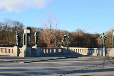 Vigelandsparken, Vigeland Sculpture Park, Frogner Park, Oslo, 27 March 2016: bronze Statue sculpture with people visiting the park in the evening  clipart