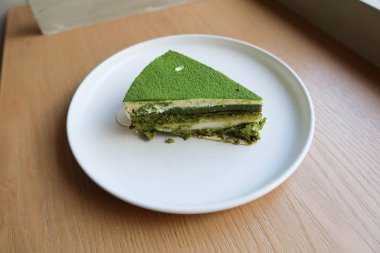 Üzerinde kibrit tozu ve beyaz mochi olan yeşil çay peynirli pastayı ahşap bir masaya koyun.