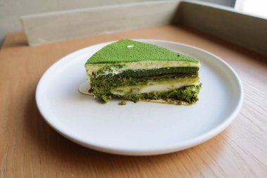 Üzerinde kibrit tozu ve beyaz mochi olan yeşil çay peynirli pastayı ahşap bir masaya koyun.