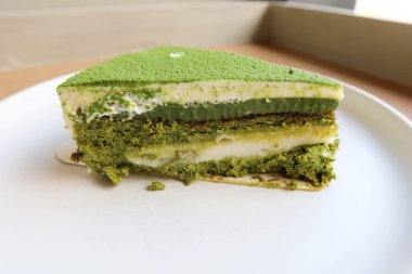 Üzerinde kibrit tozu ve beyaz mochi olan yeşil çay peynirli pastayı ahşap bir masaya koyun.