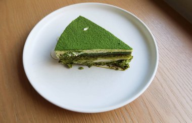 Üzerinde kibrit tozu ve beyaz mochi olan yeşil çay peynirli pastayı ahşap bir masaya koyun.