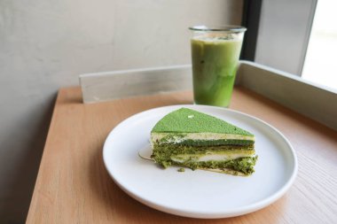 Japon kibrit peynirli peynirli keki beyaz bir tabakta mochi, buzlu yeşil çaylı latte ile ahşap bir masada, doğal güneş ışığıyla bir kafede çekilmiş.