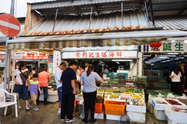 Castle Peak Bay, Tuen Mun, Hong Kong - 15 Eylül 2024: Akvaryumlarda balık ya da yengeç satın alan insanlarla birlikte deniz kenarındaki balıkçı köyündeki deniz ürünleri dükkanı