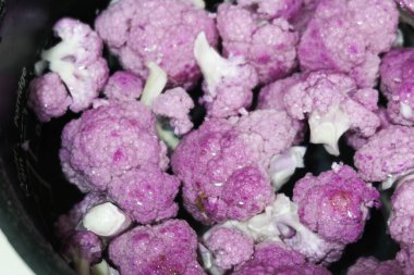 close up of purple cauliflower being washed and floating in a bowl of water ready for cooking clipart