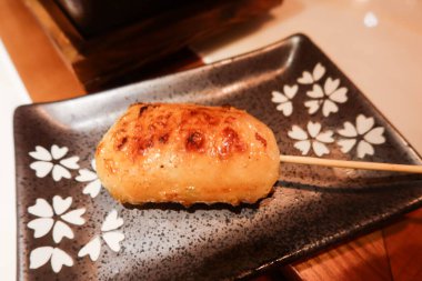 Japon kırılan ahtapot mürekkep balığı şiş kushiyaki beyaz çiçek desenli siyah bir tabakta.