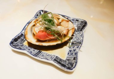 Japon izakaya restoranından alınmış tabakta bulunan kabuklu ve taze soğanlı ızgara deniz tarağını kapayın.