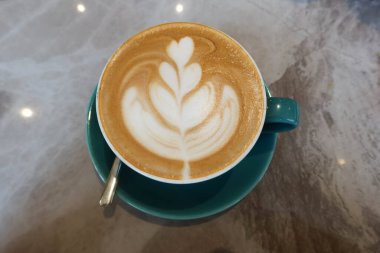 Sütlü kahve, kahve, kahve, kahve mavi bir fincanda, çay kaşığı ve mermer desenli bir masada.