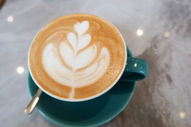 Sütlü kahve, kahve, kahve, kahve mavi bir fincanda, çay kaşığı ve mermer desenli bir masada.