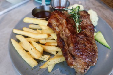 Izgara biftek, patates kızartması ve kaynamış sebzeleri tabakta yakın.