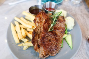 Izgara biftek, patates kızartması ve kaynamış sebzeleri tabakta yakın.