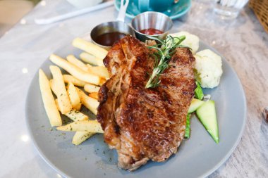 Izgara biftek, patates kızartması ve kaynamış sebzeleri tabakta yakın.