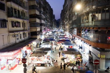 The Ladies' Market , Mong Kok, Hong Kong- 12 Oct 2024: street with hawker tent stall on both sides selling bargain clothing, food, plants, fruits, souvenirs with many people walking at night clipart