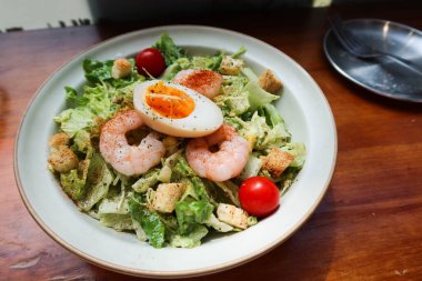 Salatayı haşlanmış yumurta, karides, vişneli domates ve beyaz tabakta avokado peyniri sosuyla kapat.