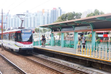 Tuen Mun Yüzme Havuzu İstasyonu, Tuen Mun, Hong Kong - 19 Ekim 2024: gündüz açık hava hafif tren istasyonu ve gündüz barınağı ile istasyona giren tramvay treni