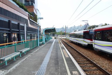 Tuen Mun Yüzme Havuzu İstasyonu, Tuen Mun, Hong Kong - 19 Ekim 2024: gündüz açık hava hafif tren istasyonu ve gündüz barınağı ile istasyona giren tramvay treni