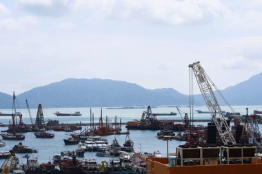 Tuen Mun İskelesi, Tuen Mun, Hong Kong - 19 Ekim 2024: Endüstriyel yük vinci gemisi arkada dağla birlikte mavi bir gökyüzünde kıyıda durdu.