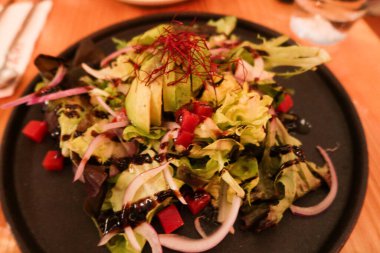 Avokado domates reçeli peyniri ve taze soğan salatasını siyah tabağa koy.