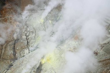 Owakudani, Japonya- 29 Ekim 2024: Dağ boyunca duman ve teleferikli volkan dağı, sarı, kahverengi ve turuncu renkli kayalar, otoban manzaralı.