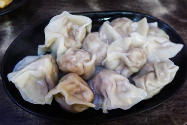 Çin Tayvan usulü haşlanmış hamur köfteleri, sebzeler ve siyah tabakta domuz dolgusu.