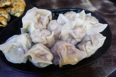 Çin Tayvan usulü haşlanmış hamur köfteleri, sebzeler ve siyah tabakta domuz dolgusu.