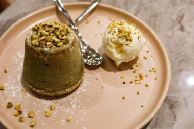 Tatlı şam fıstıklı lav keki, yanında vanilyalı dondurma ve iki kaşıklı fındık.