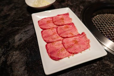 Japon çiğ kırmızı sığır etini dilimle dilimleyip beyaz tabakta altı parça halinde yakiniku restoranındaki ocağın yanında ızgara yapmaya hazır hale getireceğim.