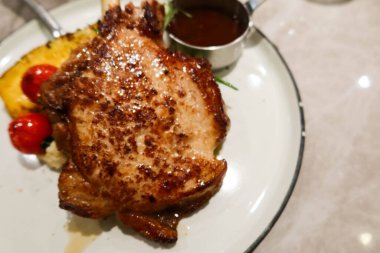 Tavada kızartılmış domuz filetosu ve bonbon. Yanında ananas ve vişneli domates ve barbekü sosu. Büyük beyaz bir tabakta, fotokopi alanı ile.