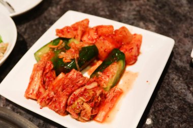 Aperatif olarak beyaz bir tabakta mayalanmış Kore kimchi, havuç ve salatalık yakın çekim 