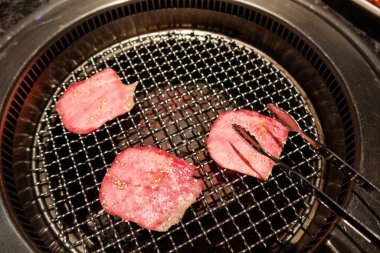 close up of Japanese three pieces of grilling raw uncooked red ox beef tongue with clip in a glove clipart