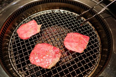 Japon usulü ızgarada pişmemiş üç parça çiğ sığır eti diliyle eldiven tak.