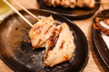 Bir restoranda siyah bir tabakta iki parça ızgara Japon tavuk kanadı şiş (yakitori).