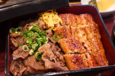 Japon yemek çantasını (bento) yarım ızgara yılan balığı pilavı ve yarım wagyu bifteği ile kapatın. Miso çorbası yanında, başlangıç ve kırmızı kaşık.