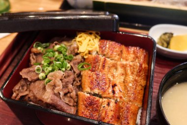 Japon yemek çantasını (bento) yarım ızgara yılan balığı pilavı ve yarım wagyu bifteği ile kapatın. Miso çorbası yanında, başlangıç ve kırmızı kaşık.