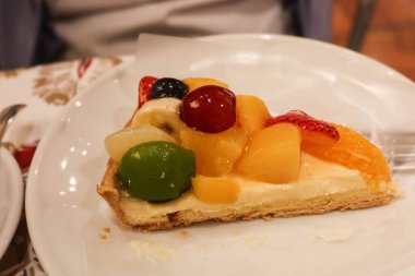 Bir dilim meyveli turtayı muhallebi, üzüm, mango, şeftali ve kremayla kaplayın.