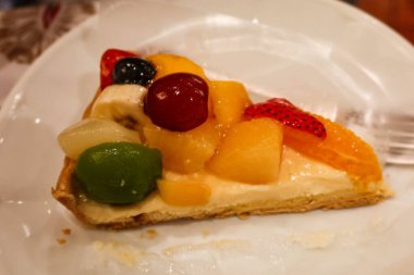 Bir dilim meyveli turtayı muhallebi, üzüm, mango, şeftali ve kremayla kaplayın.