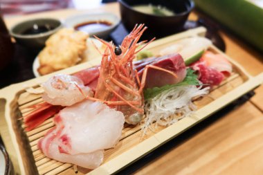 Japon saşimi çeşitlerine yakın karides, karides, balık, somon, levrek ve balık dilimlenmiş ahşap tabakta.