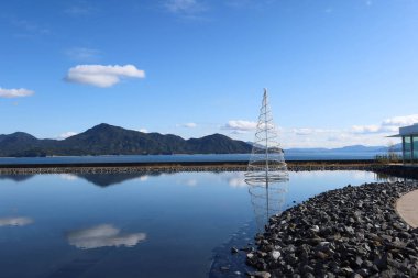 Simose Art Museum, Hiroshima, Japan- 13 Dec 2024: Art Museum in blue colour with reflection of water and a Christmas tree in da clipart