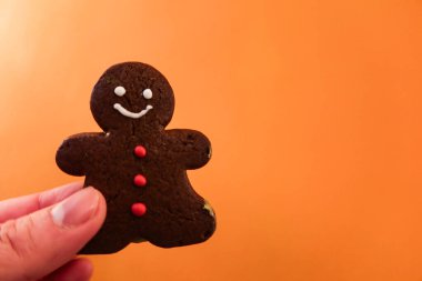 Noel için turuncu arka plan duvarında zencefilli bisküvi tutarken parmağını kapat.