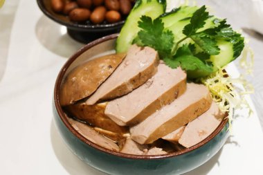 close up of Chinese Hong Kong Chaozhou style marinated goose liver foie gras slice with cucumber on the side in a blue bowl clipart