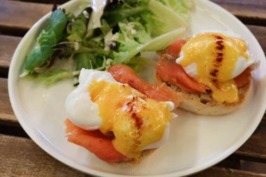Benedict usulü yumurtalı, somon balıklı ve kremalı kek ekmekli İngiliz kahvaltısı. Tahta bir masada beyaz bir tabakta salata sebzeleri (yumurta kraliyet ailesi))