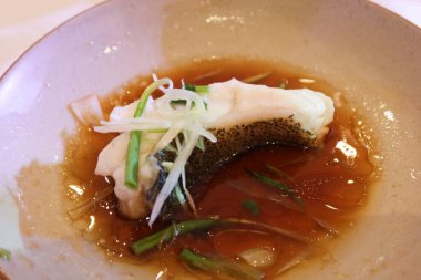 Çin usulü Hong Kong usulü soya soslu bir balık dilimi, taze soğan ve bir tabakta pişmiş yağ sosu.