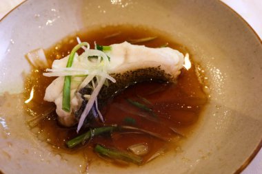 Çin usulü Hong Kong usulü soya soslu bir balık dilimi, taze soğan ve bir tabakta pişmiş yağ sosu.