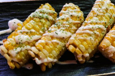 Izgara mısırın dörtte birini kapat. Siyah tabakta salata sosu ve yosun ekle.