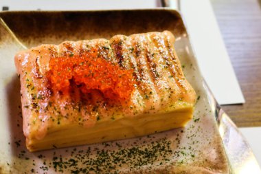 Dikdörtgen Japon omleti (Tamagoyaki), somon yumurtası (ikura) ve yosun tozu ile yakın plan.