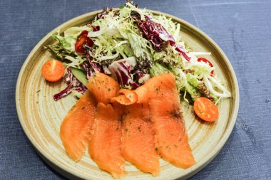 Dört dilim çiğ somon balığı salatası, vişneli domates ve gri izole arkaplanda karışık yeşil.