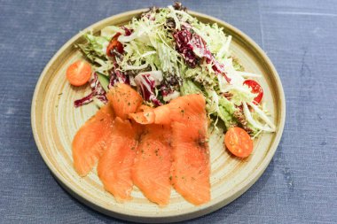 Dört dilim çiğ somon balığı salatası, vişneli domates ve gri izole arkaplanda karışık yeşil.