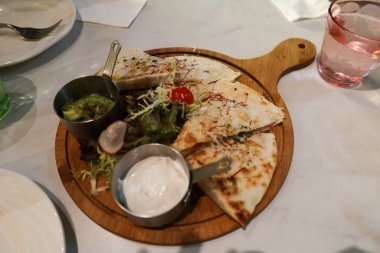 Quesadilla ya da vantilatör şeklinde birkaç dilim ekmek ve iki küçük metal kase ekşi krema sosu ve saplı ahşap servis tahtasına daldırmak için guacamole.