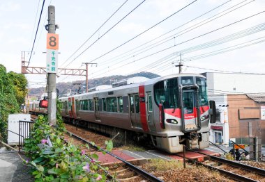 Onomichi, Hiroşima, Japonya- 9 Aralık 2024: Demiryolu hattından geçen tren halatlar asılı ve diğer tarafta evler var.