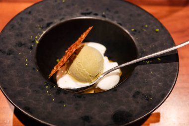 Soğuk yeşil çaylı dondurmayı yanına çıtır bisküvi ve çay kaşığıyla siyah bir tabakta krema ile kapat.